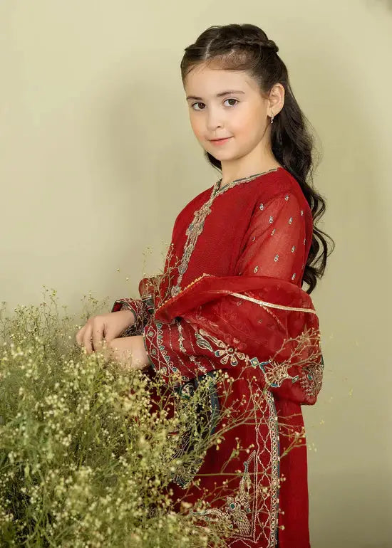 a young girl in a red dress standing next to a bush