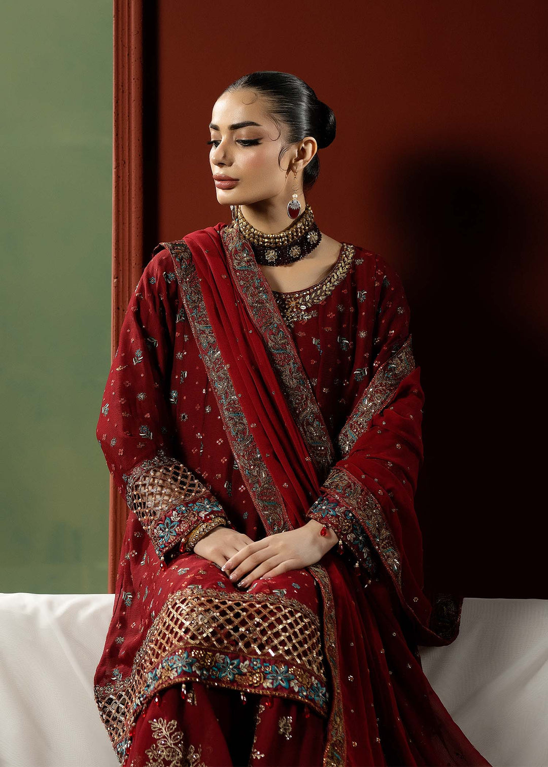 Seated model in RANGREZA RED red colour dresses pakistani showcasing embroidered chiffon dupatta and traditional sharara in Bangladeshi fashion.