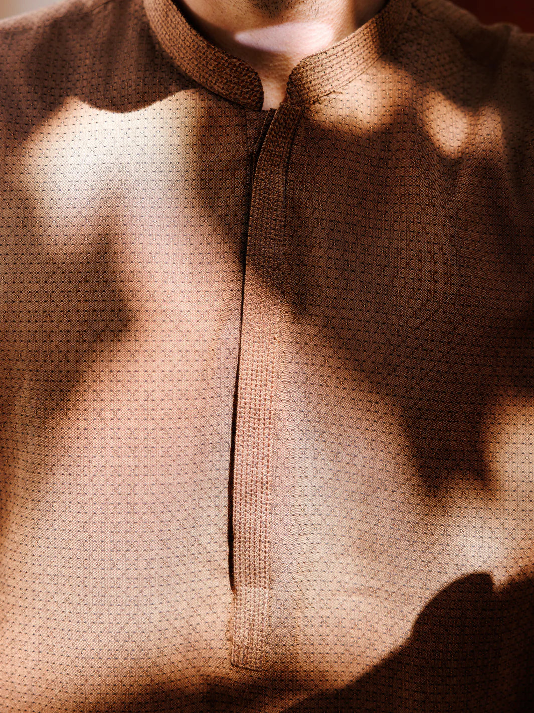 Man wearing brown kurta with sunglasses, standing near mosaic wall, stylish pose