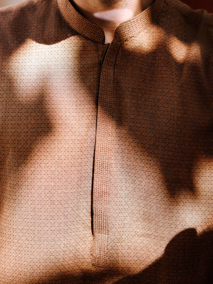 Man wearing brown kurta with sunglasses, standing near mosaic wall, stylish pose