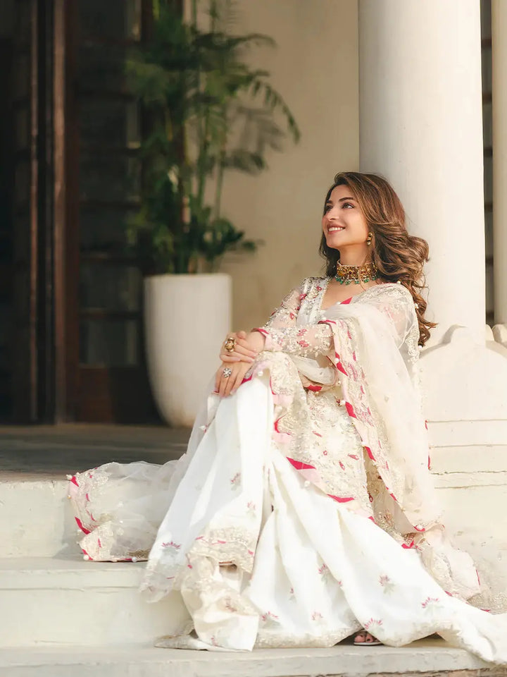 Elegant white embroidered sharara with red accents and intricate embellishments, paired with a matching dupatta, perfect for wedding occasions