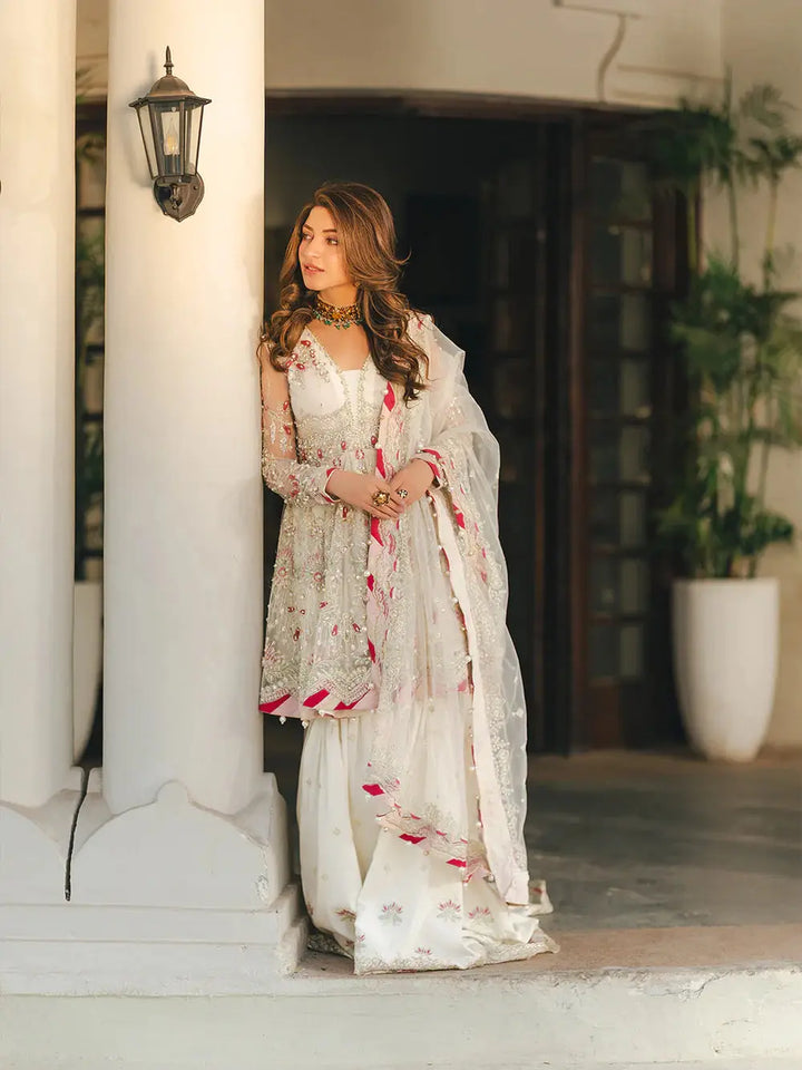Beautiful woman in white embroidered traditional dress with intricate embellishments, wearing jewelry, standing near a column for wedding or festive occasion
