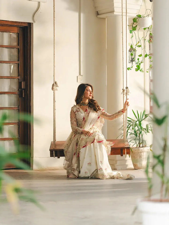 Elegant bridal outfit with embroidered net fabric, sequin work, pearls, and dabka detailing, on a wooden swing