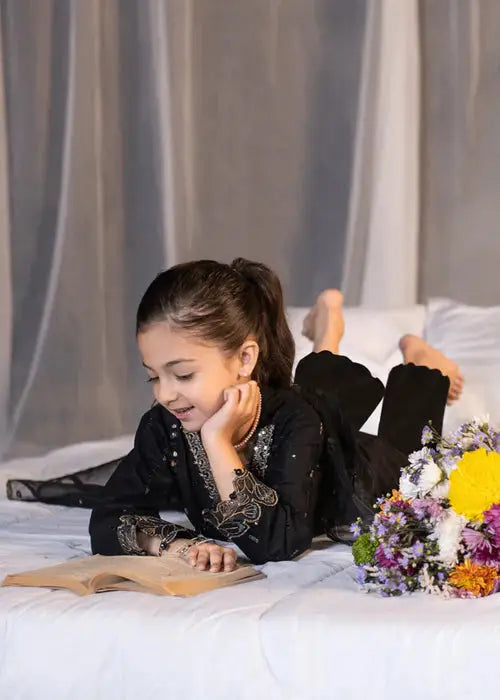 Young girl in black traditional dress reading a book on bed with flowers