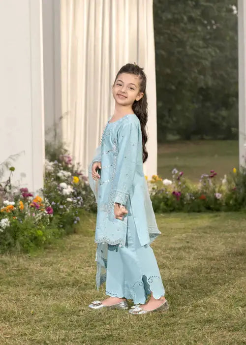 Smiling girl in light blue embroidered dress, standing in garden with flowers, side view