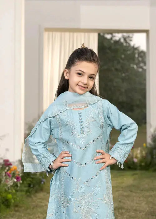 Girl in embroidered light blue dress with dupatta, posing indoors with curtains and garden view