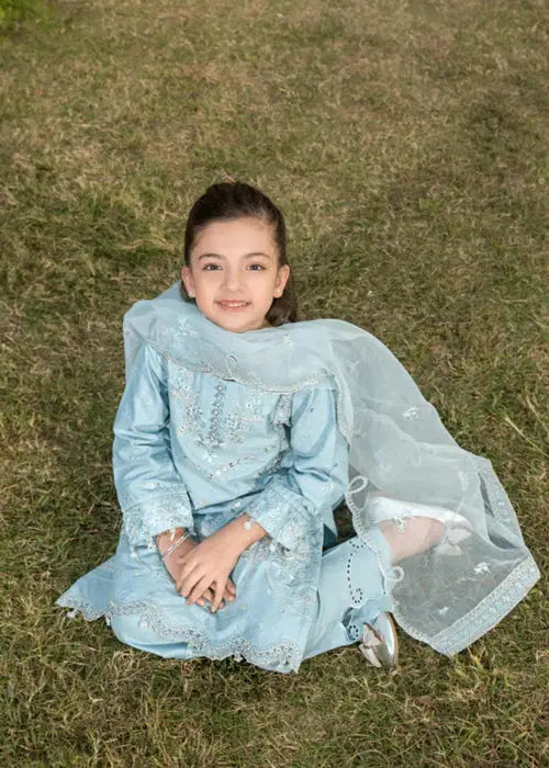 Girl sitting on grass in light blue embroidered dress with dupatta, smiling