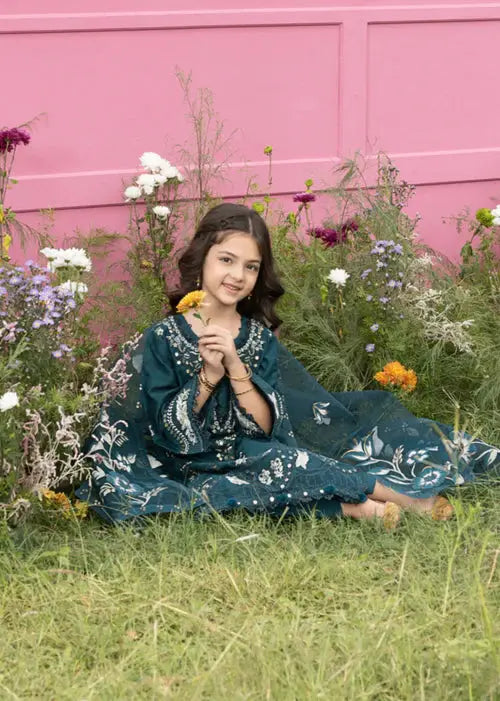 Girl sitting on grass in dark green embroidered dress with flowers and pink wall