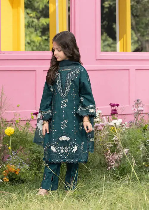 Side view of girl in embroidered dark green dress with pink wall and garden backdrop