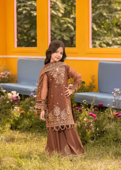 Girl in brown embroidered dress with dupatta, standing in floral garden with yellow wall background