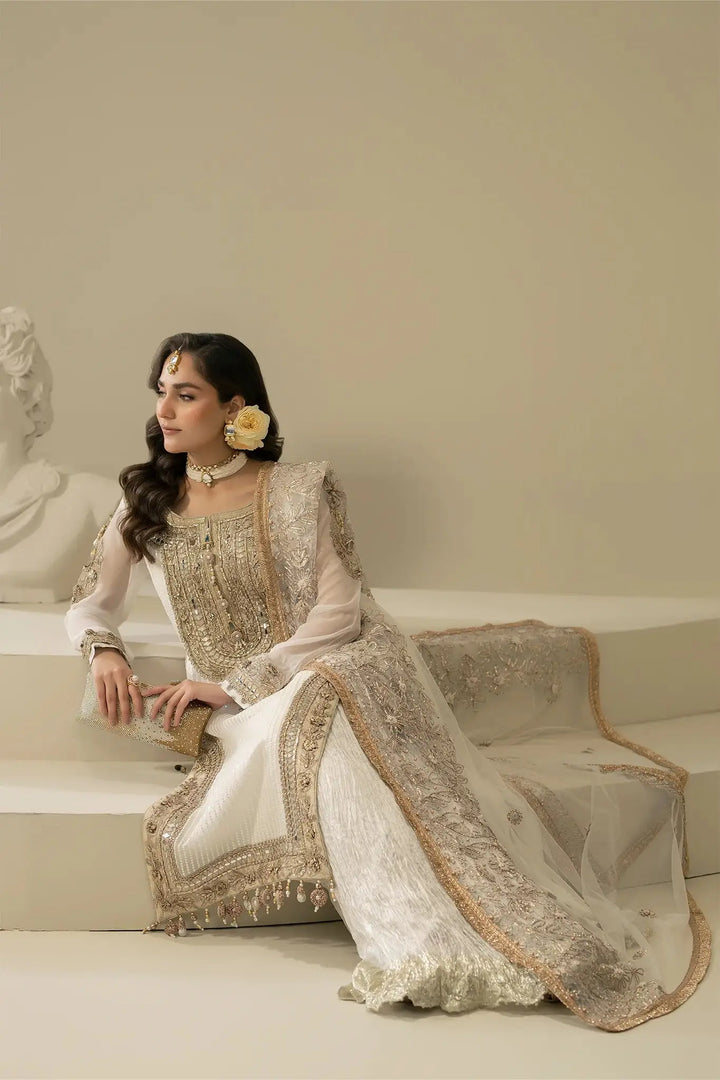 Model seated in M-109 OFF-WHITE Pakistani ensemble with luxurious hand embroidery, perfect for festive and formal wear.