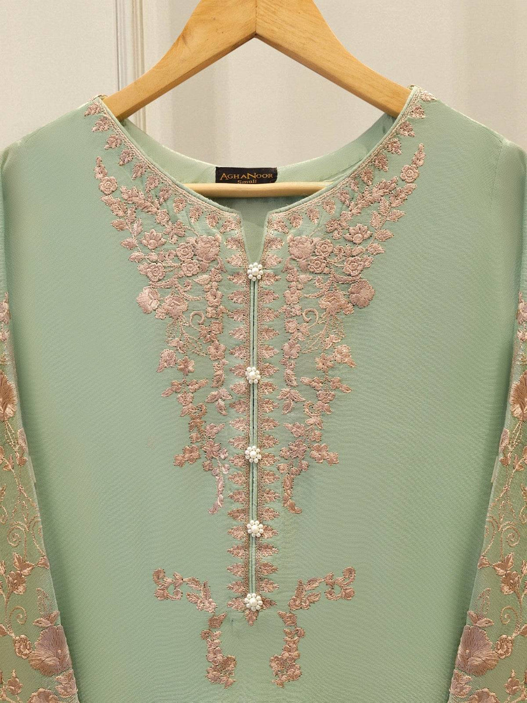 Close-up of AGHA NOOR embroidered neckline with pearl buttons and floral detailing on cotton net, highlighting craftsmanship and luxury.