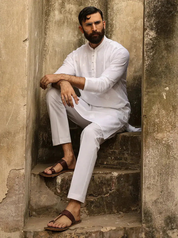 Man in white embroidered kurta with fabric buttons, sitting on rustic stairs