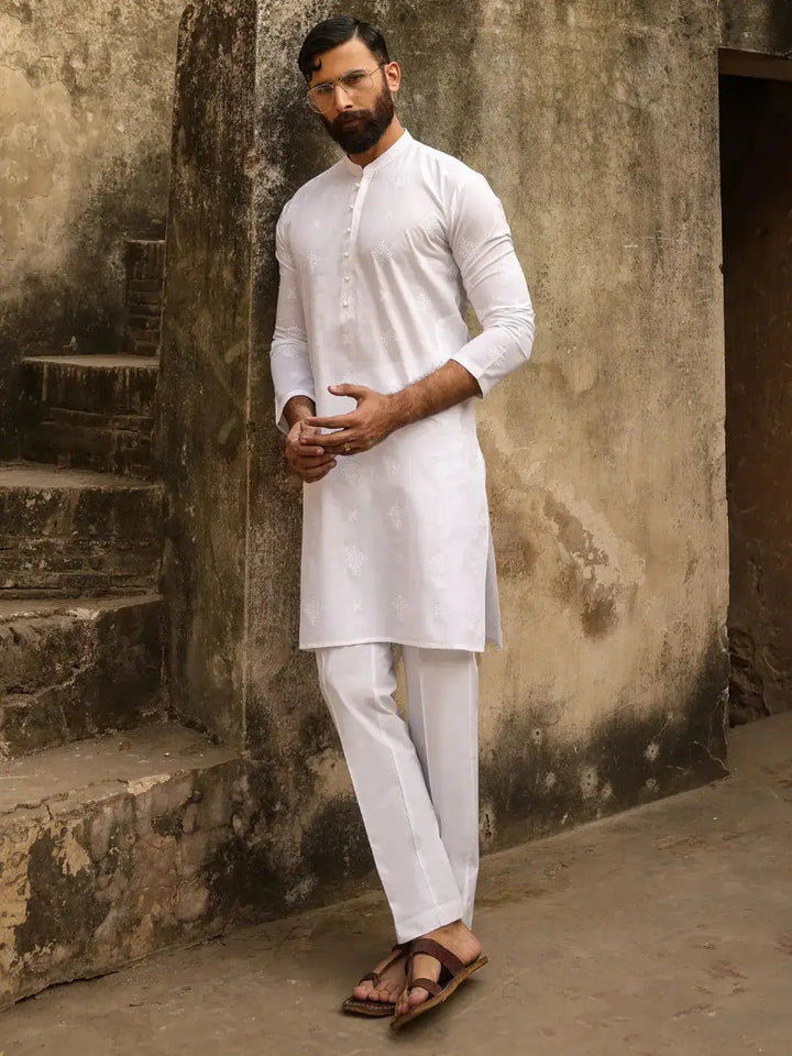 Man in white embroidered kurta with fabric buttons, standing on rustic stairs