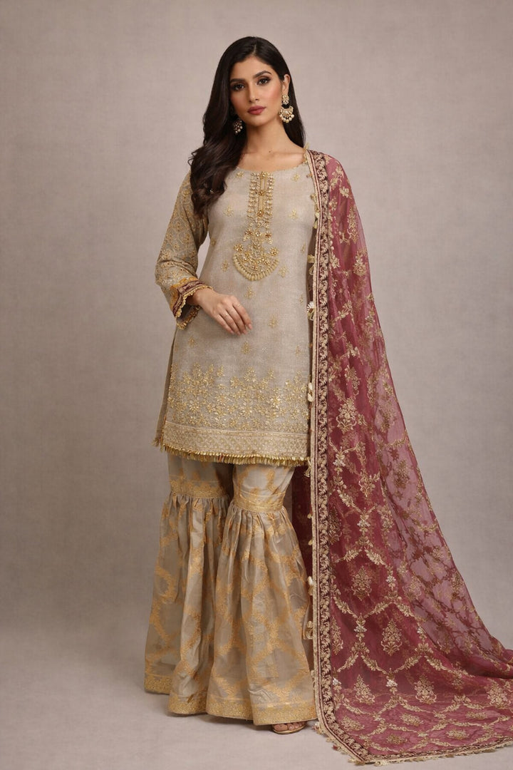 Woman wearing a traditional outfit with gold embroidery and a maroon dupatta on a neutral background