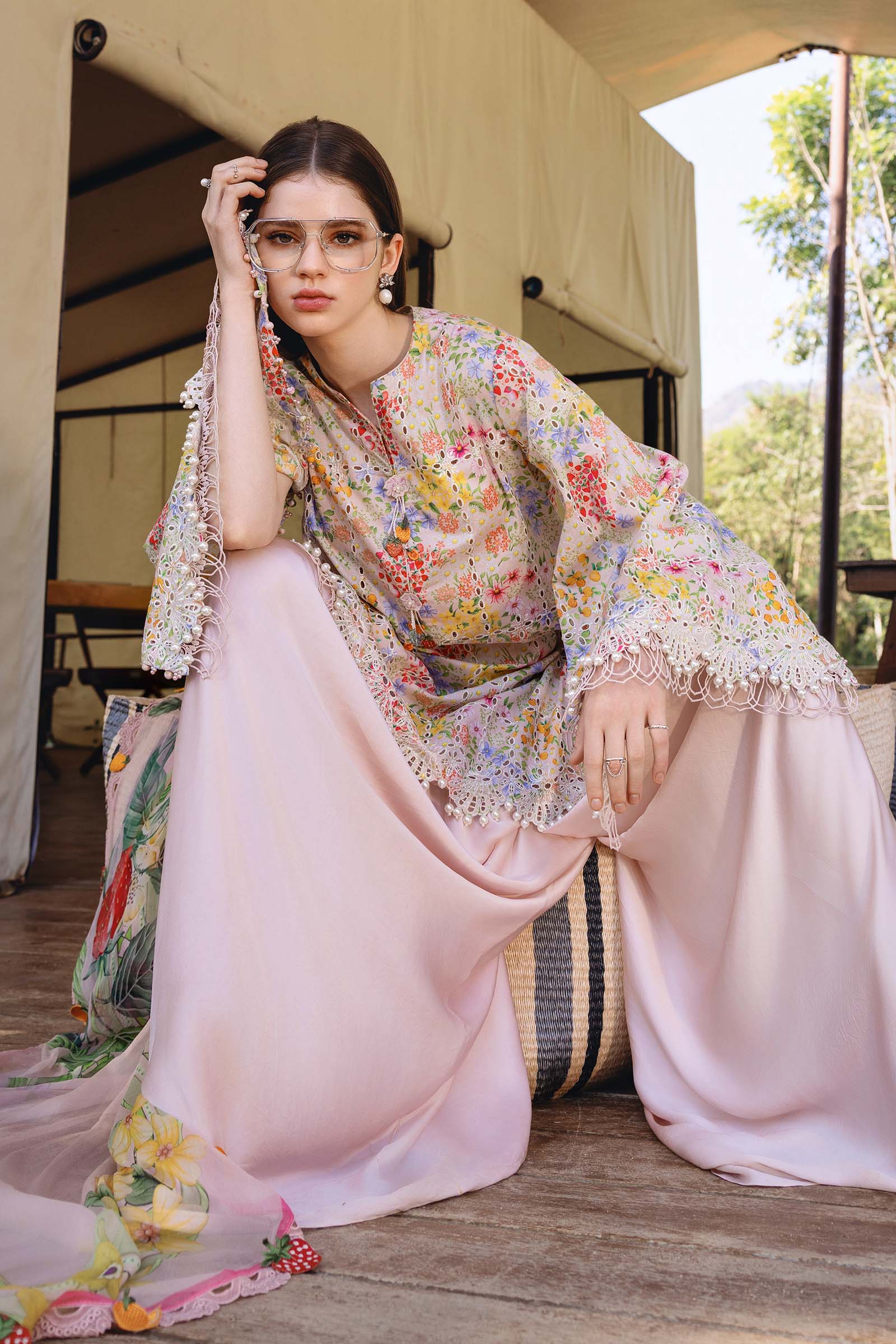 Woman in a floral kimono-style top and pink skirt sitting outdoors.
