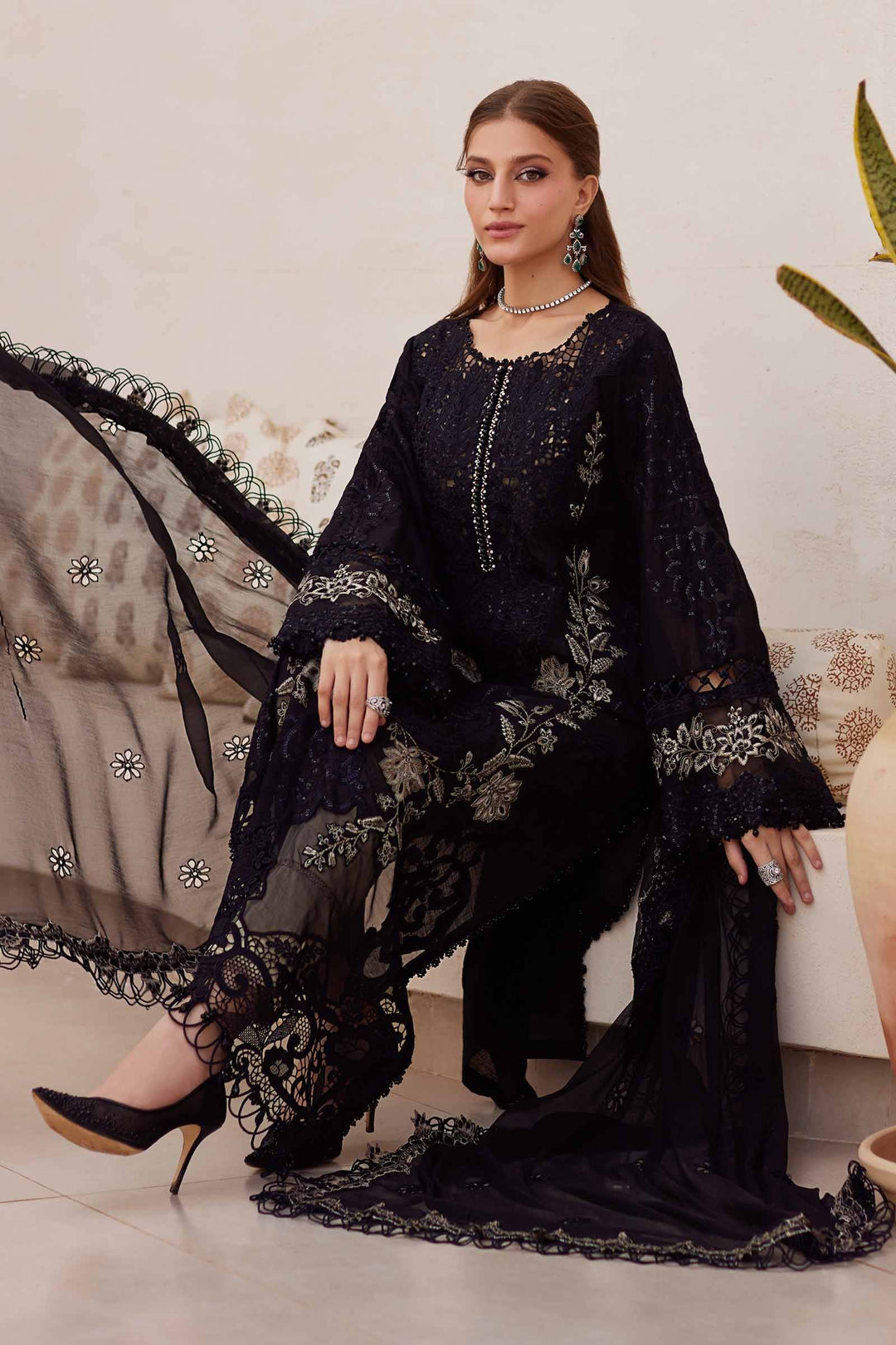 Model seated in AL-4312 black embroidered 3 piece suit with flowing chiffon dupatta and cambric trousers, styled for formal events.