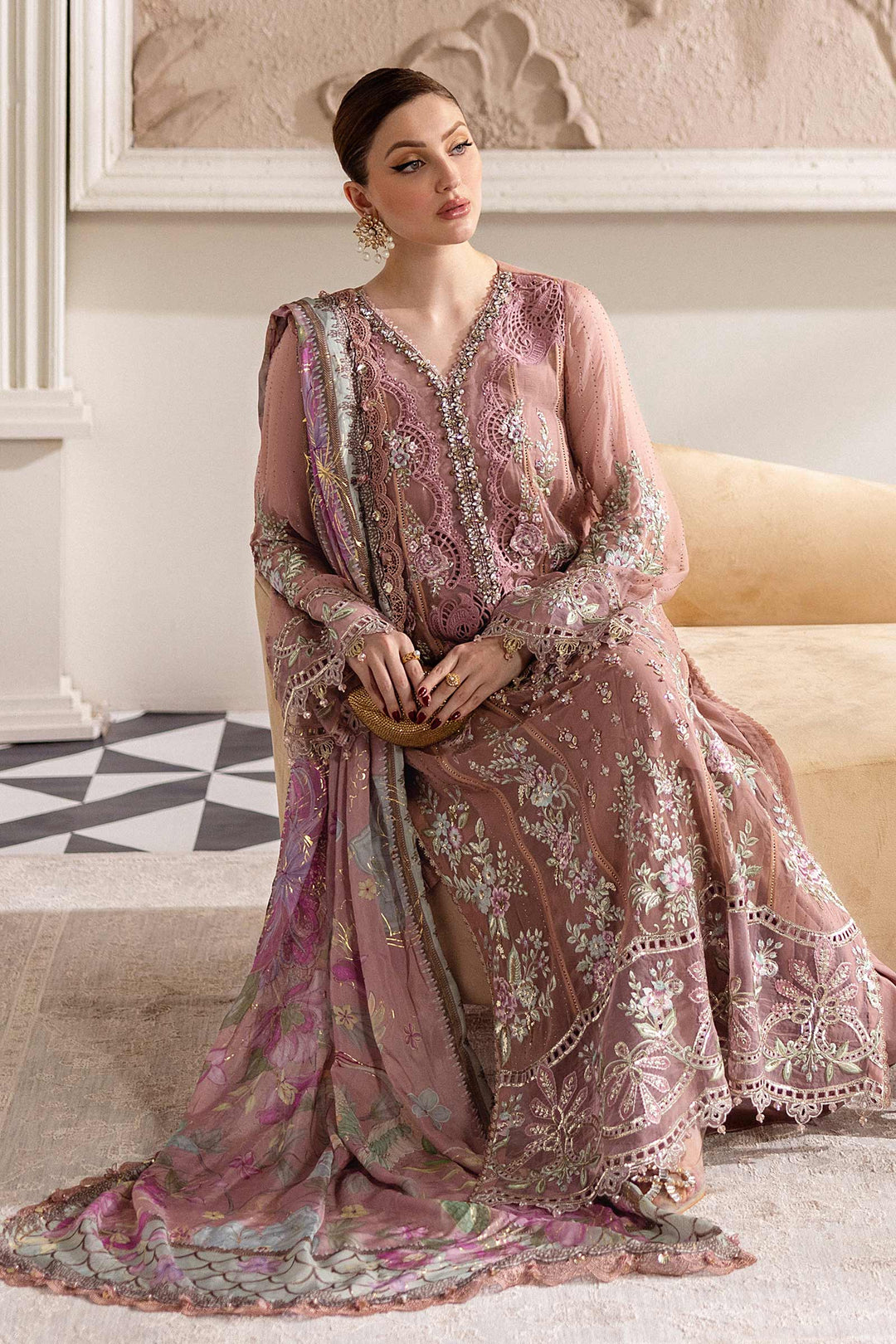 Seated model in MARIA.B MPC-25-105 embroidered chiffon suit featuring pastel floral motifs and organza accents for formal wear.