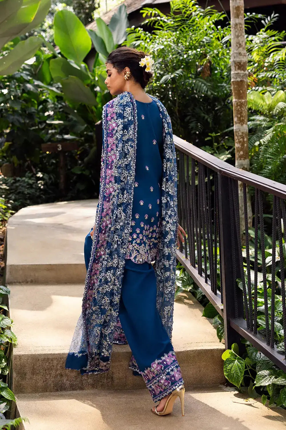 Back view of DELARA-SRF25-08 royal blue silk suit by SAIRA RIZWAN LUXURY, showcasing floral embroidery and sheer dupatta in outdoor greenery.