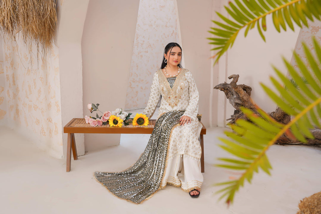 Model seated in RANGREZA SAJNI festive dress with floral decor, showcasing full outfit including shirt, pants, and dupatta.
