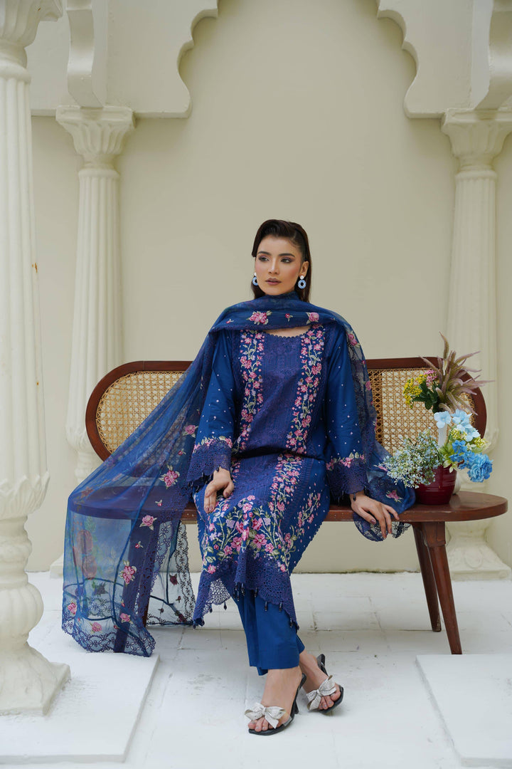 Seated model in RANGREZA SAJNI RS-3518-1000 blue Pakistani suit with floral embroidery and dupatta, styled for a traditional festive occasion.