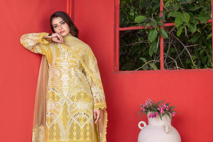 Model wearing RANGREZA SAJNI RS-3503-1200 yellow Pakistani dress with embroidered shirt and dupatta, leaning against red wall.