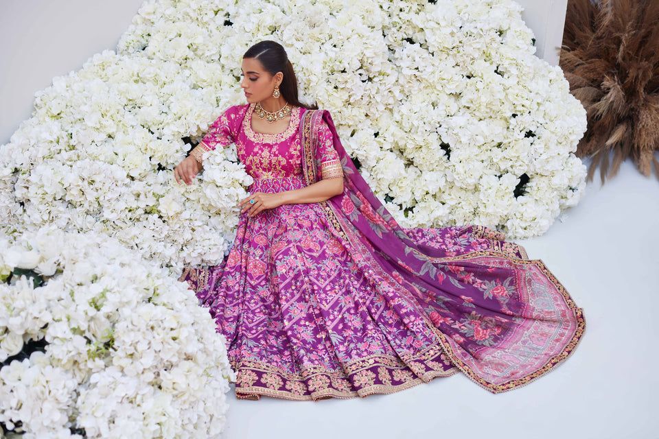 Mina Hasan pink floral embroidered outfit with dupatta, model reclining elegantly on a bed of white flowers in a luxurious setting.