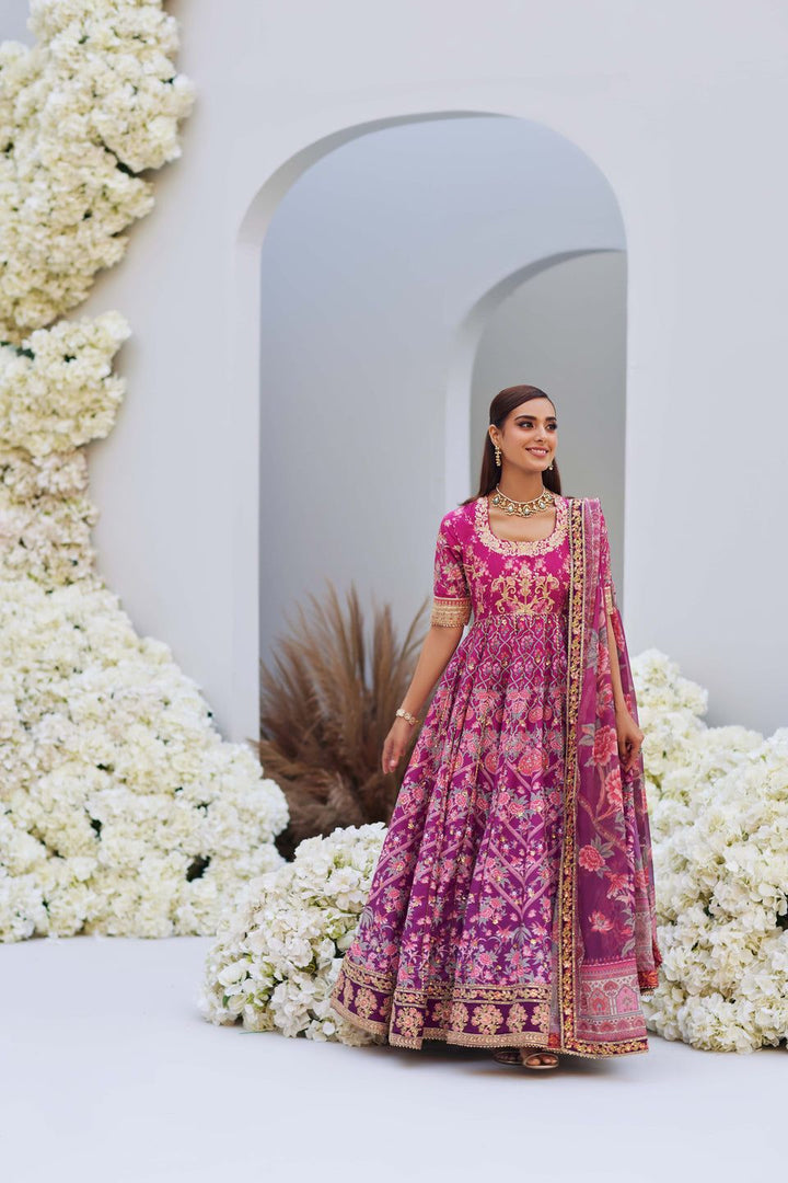 Mina Hasan pink ombre floral embroidered outfit with dupatta, model standing elegantly in a floral archway setting.