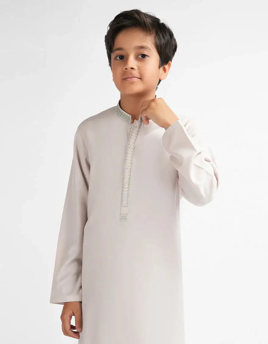 Young boy wearing a light gray kurta with white details on a white background
