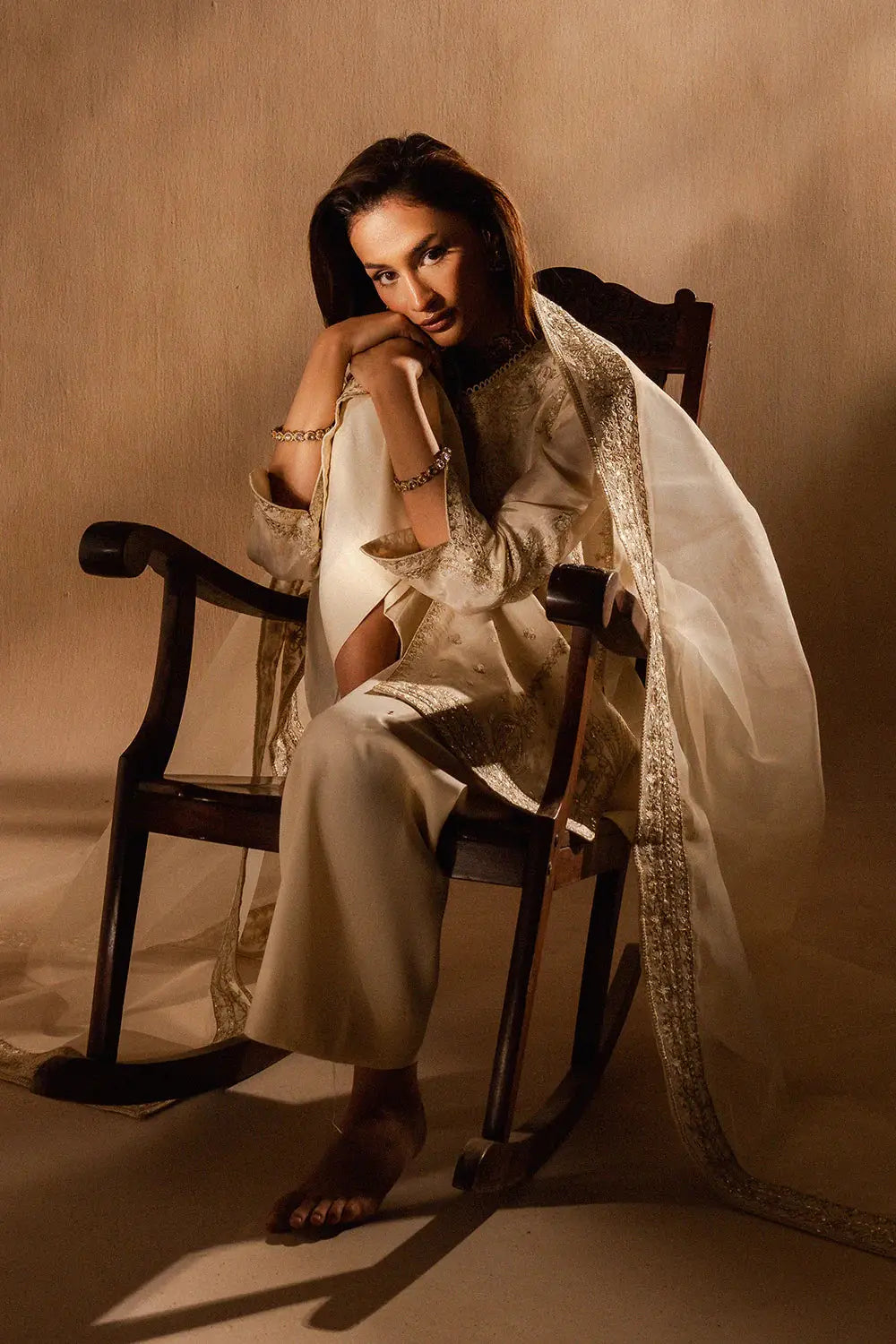 Seated model in Maryum Alice Outfit - Mariam's Collection, displaying luxurious beige organza fabric with delicate embroidery in a relaxed pose.