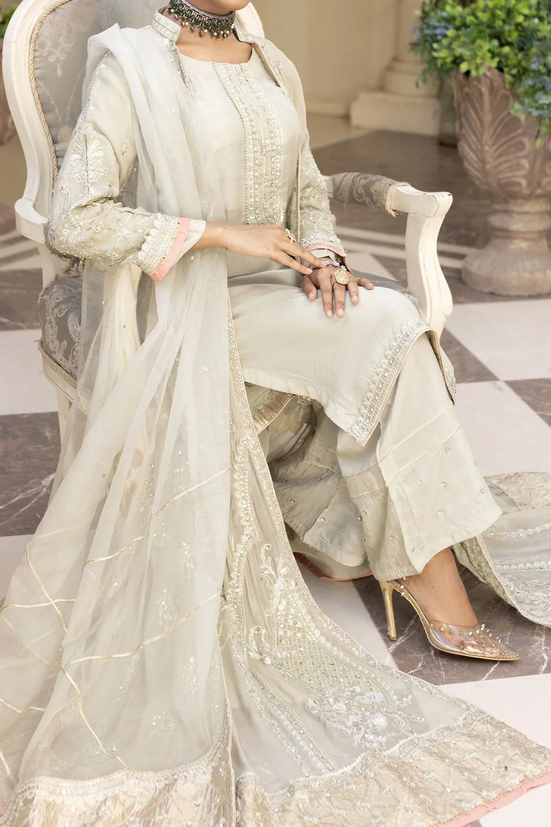 Close-up of seated woman in light grey Pakistan gown dress with embellished dupatta and pants, ideal for festive wear.