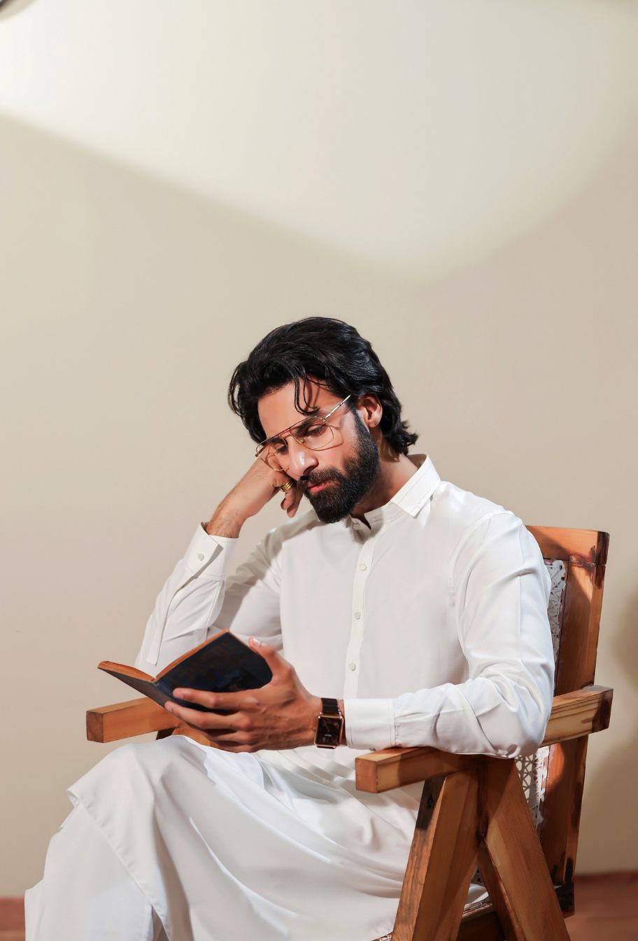 Man in white traditional attire sitting on a wooden chair holding a black book.