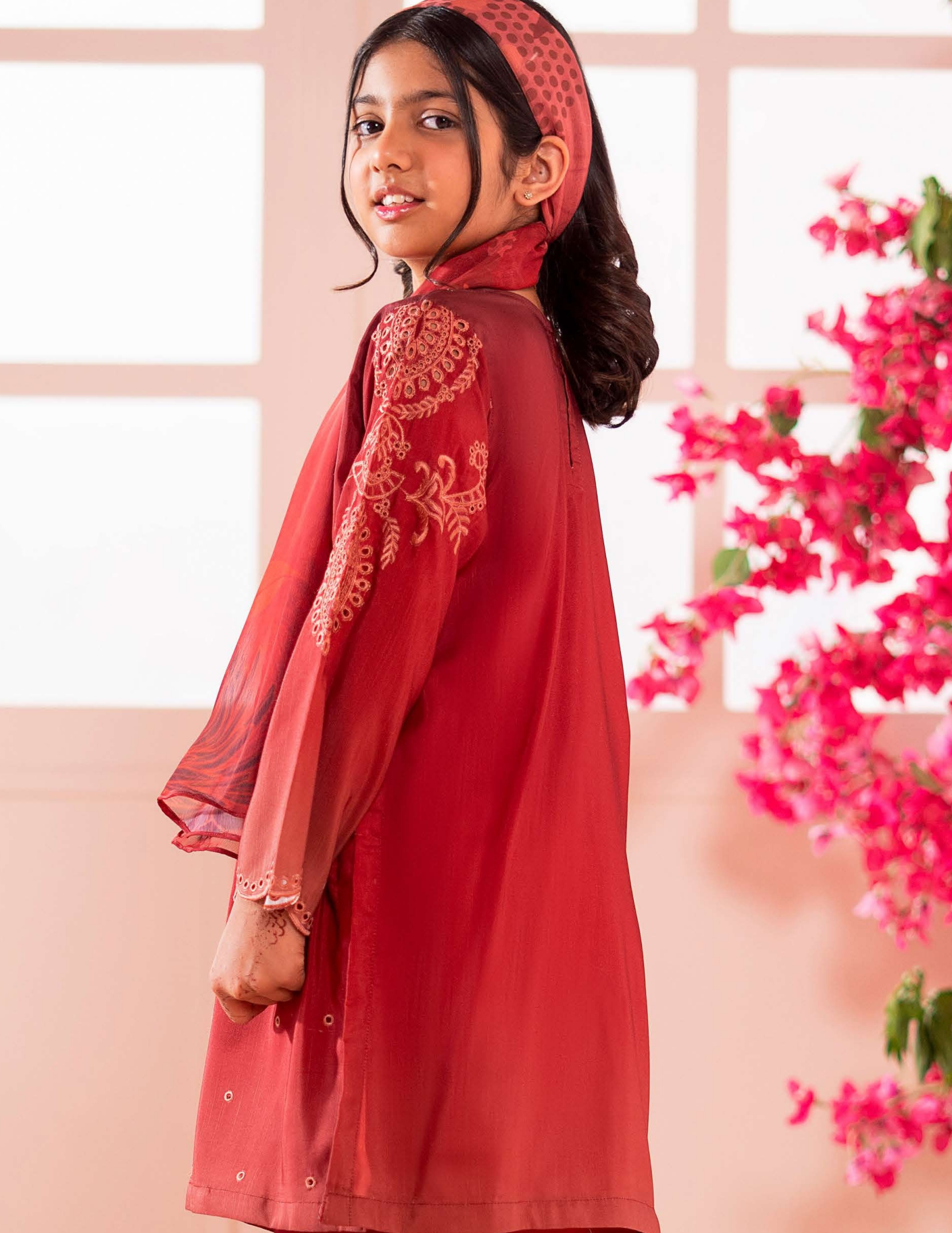 Young girl wearing a red traditional outfit with floral patterns against a pink floral background