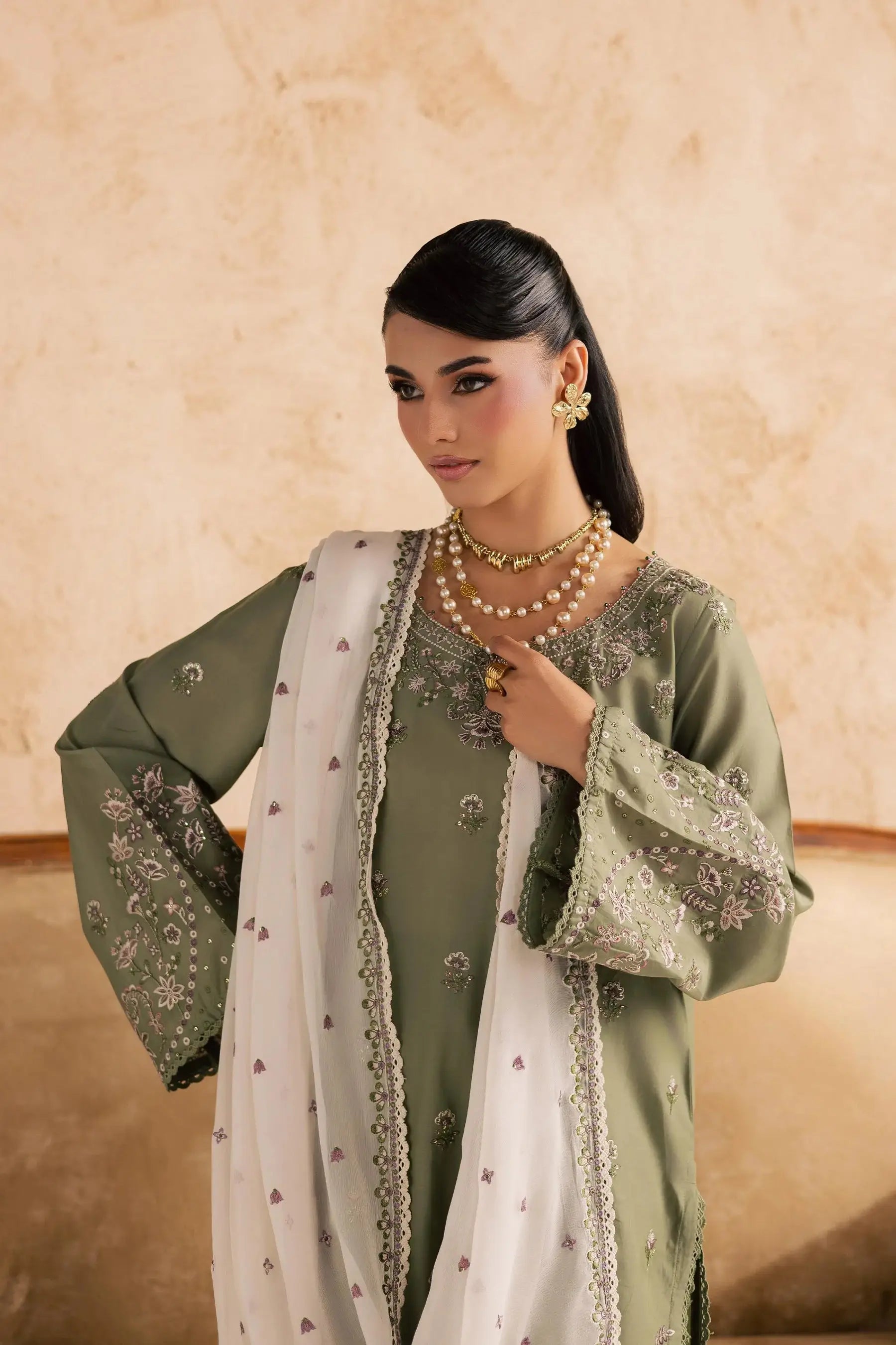 Woman wearing a green traditional outfit with a white dupatta against a beige background