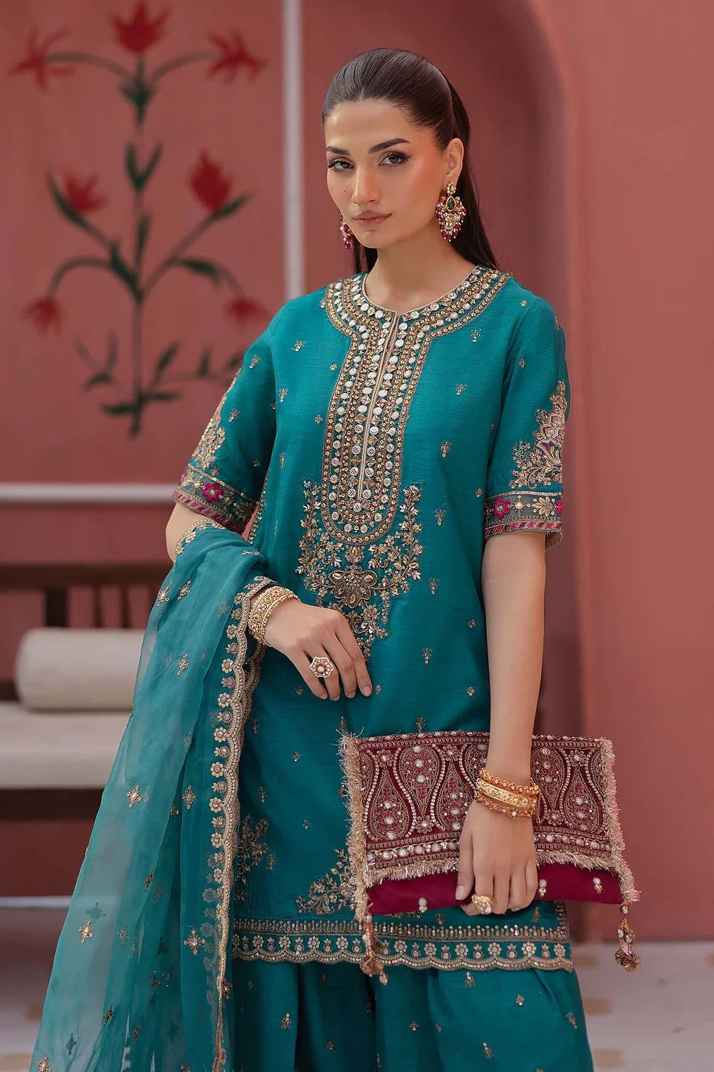 Woman in a teal traditional outfit with intricate embroidery in a decorative setting.