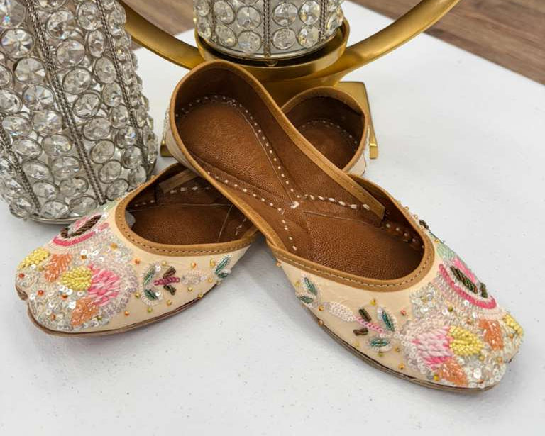 Pair of embroidered flats with floral patterns on a white surface, with decorative vases in the background.