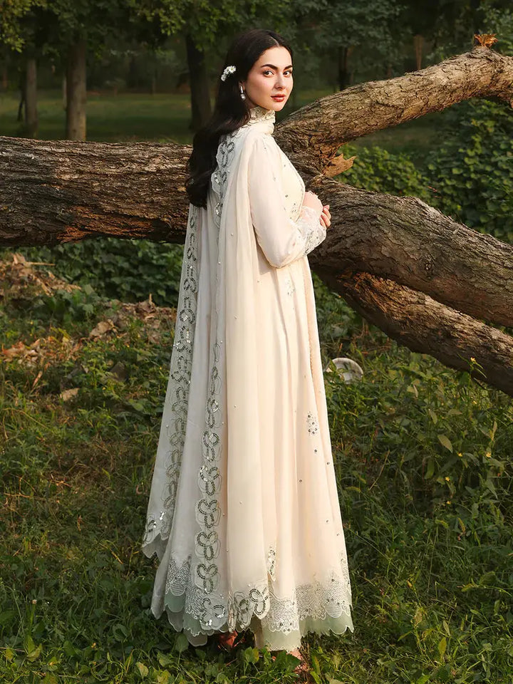 Side view of woman in cream embroidered dress with dupatta, floral border, and lace, outdoors in greenery