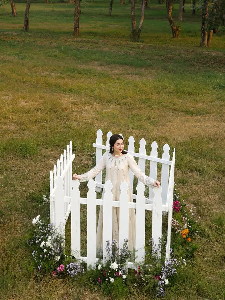 Model in cream embroidered dress outdoors with white picket fence