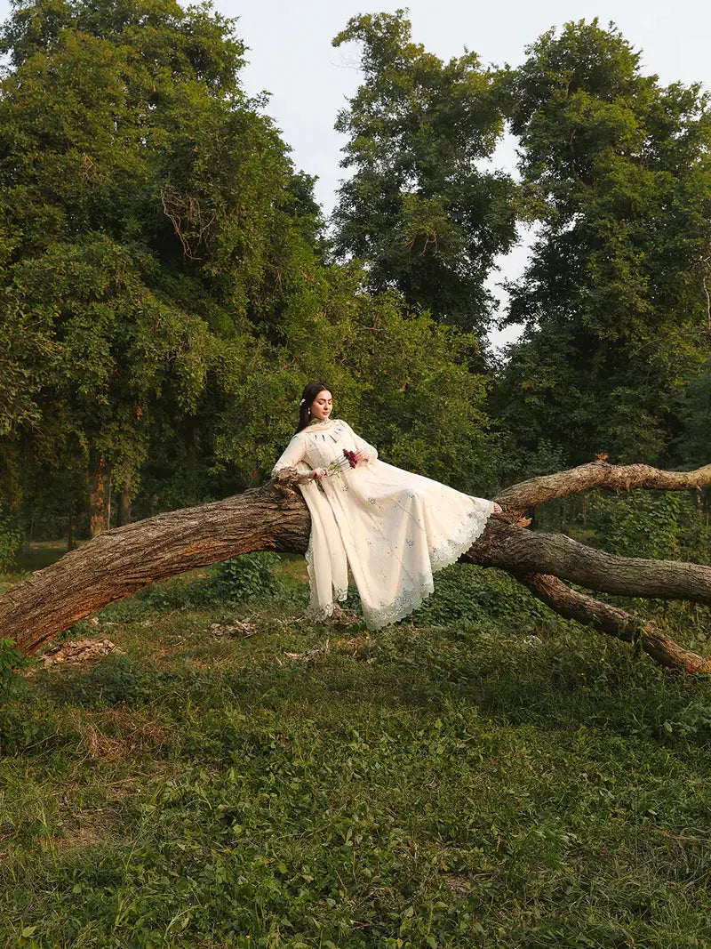 Model sitting on tree branch in cream embroidered dress