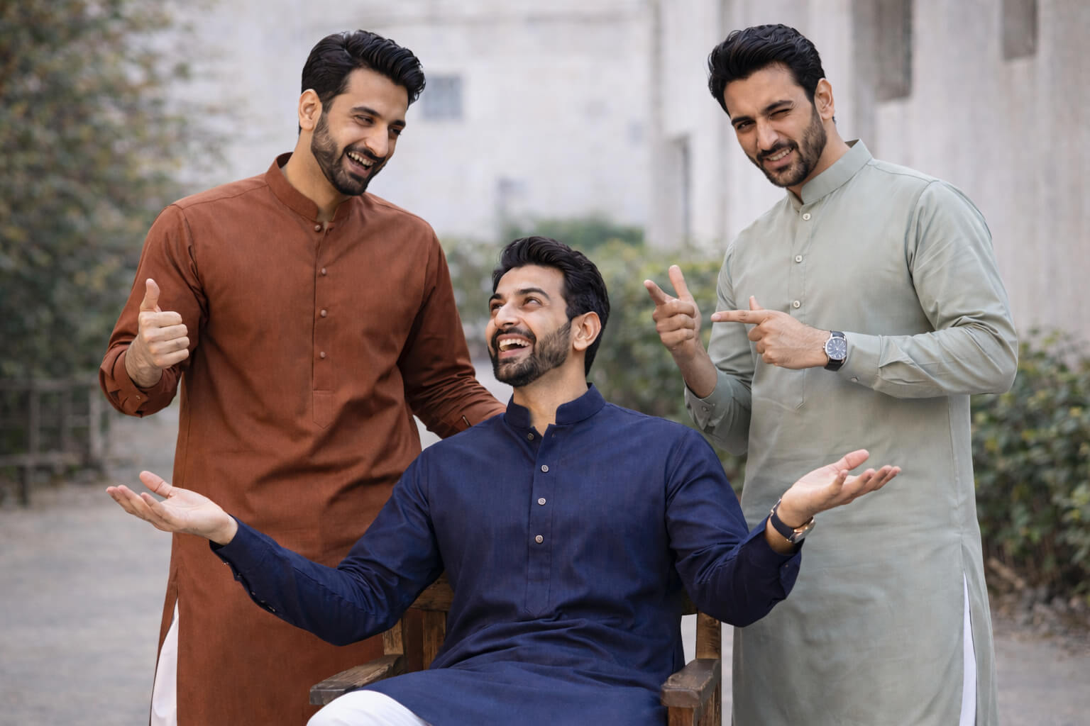 Three men in traditional attire posing outdoors with a neutral background