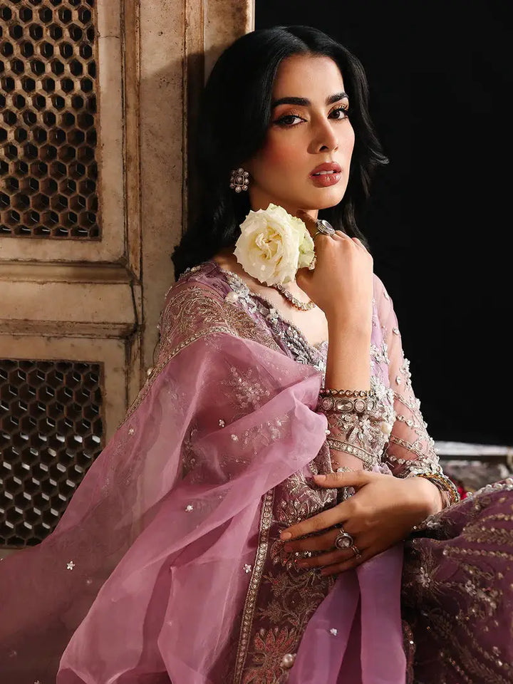 Close-up of model wearing pink embroidered dress with jewelry, holding a white flower, highlighting intricate embroidery and accessories