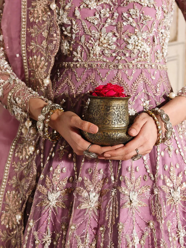 Model holding a decorative brass pot with rose petals, dressed in pink embroidered attire with jewelry, showcasing traditional elegance