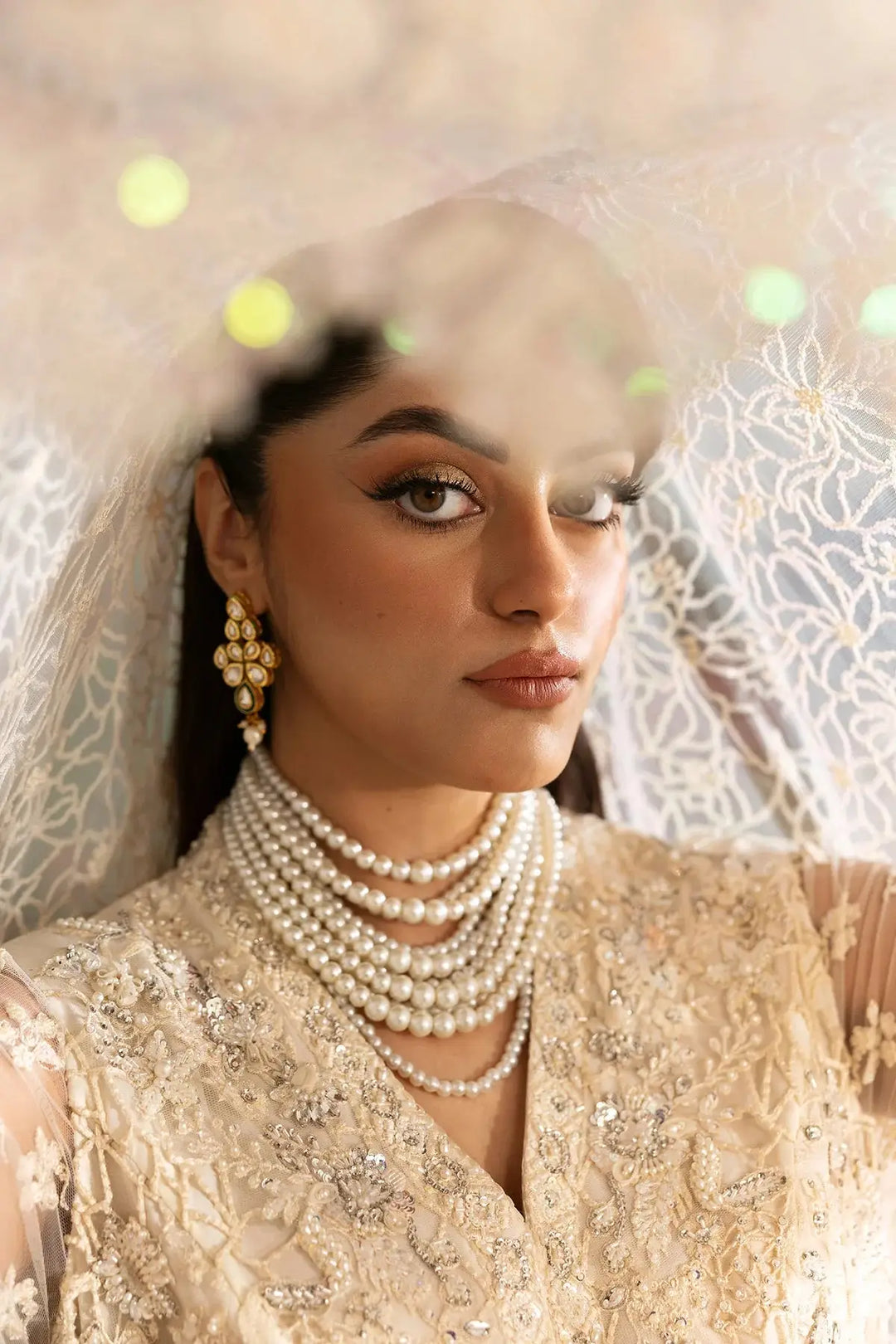 Close-up of model wearing pearl jewelry and embellished neckline of Pakistani bridal dress, highlighting intricate hand embroidery details.