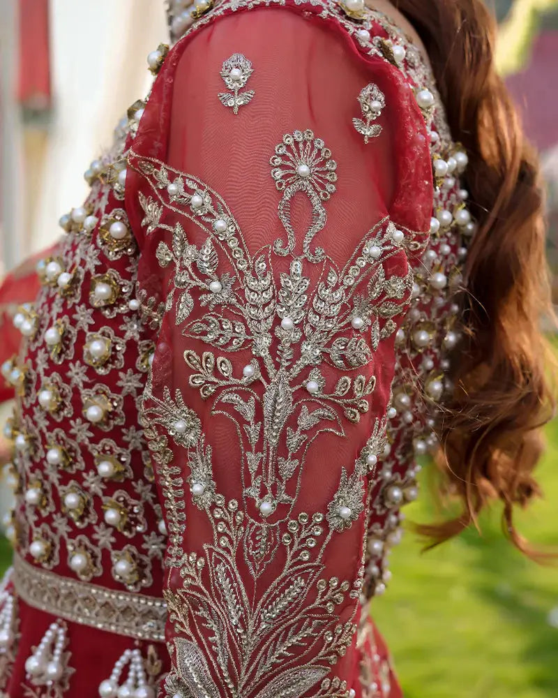 Close-up of AROOSH Wedding Wear sleeve embroidery with floral motifs and pearl embellishments on sheer red organza fabric.