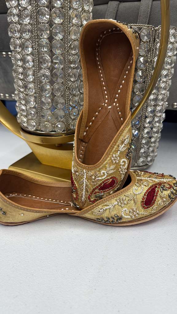 Shop Roshni Golden Festive khussa shoes for ladies featuring gold base with red zari paisley embroidery, ideal for weddings and traditional events.