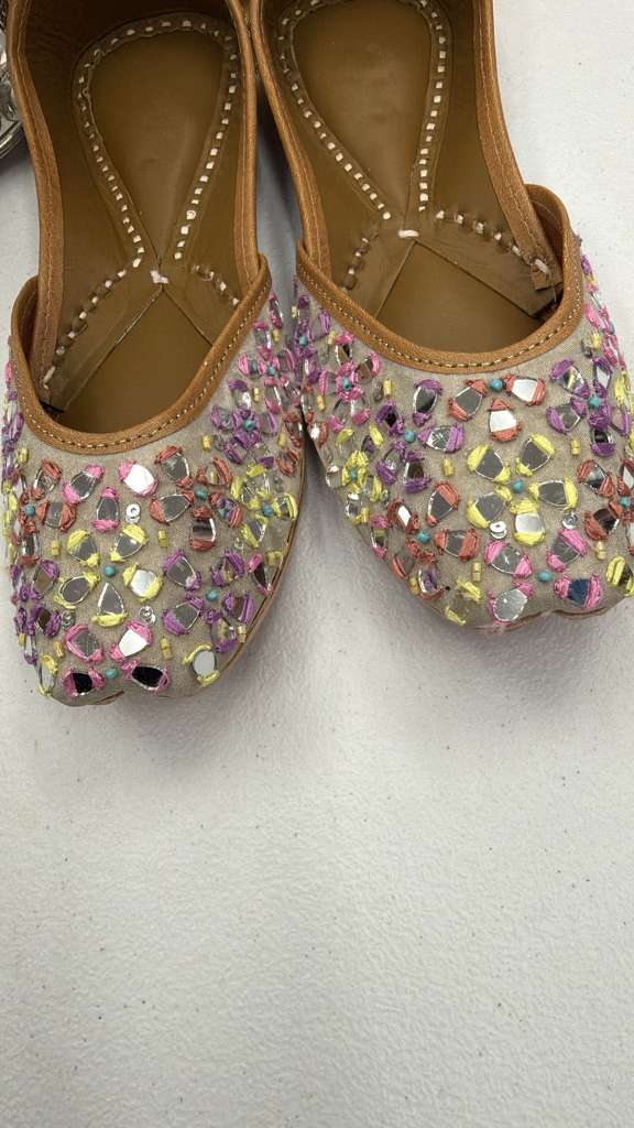 Close-up of Sheesha Golden Jutti showcasing intricate mirror embroidery on soft beige base. Elegant flat footwear for festive and ethnic outfits.