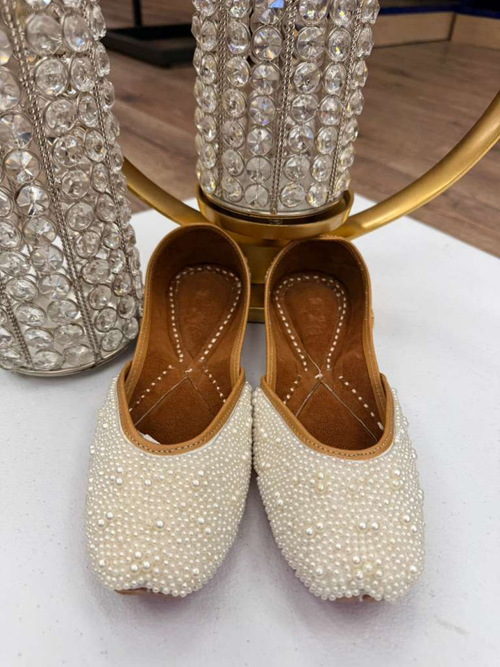 Front view of pearl-embellished white Khussa Jutti for weddings, placed near crystal decor. Perfect traditional slip-on shoes for brides.