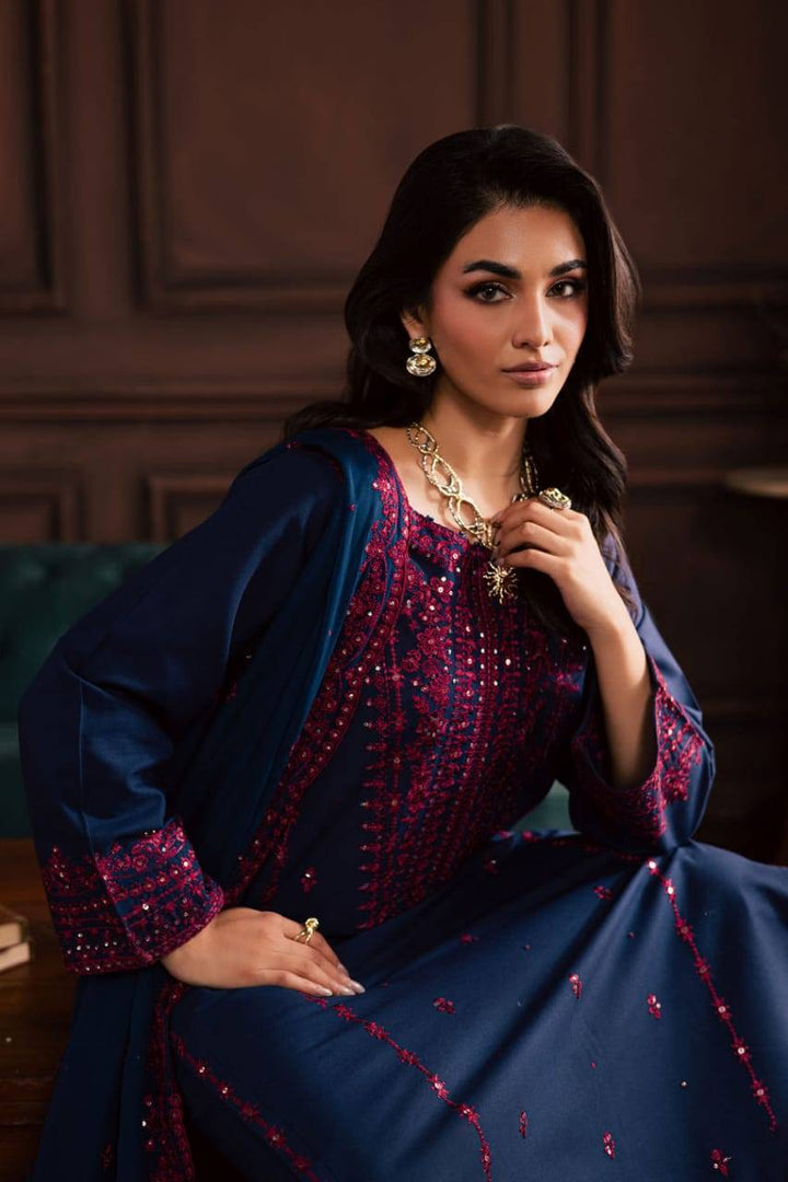Model seated in BATIK Lamia 3Pc embroidered khaddar dress, highlighting the rich pink embroidery on the navy fabric for a festive look.