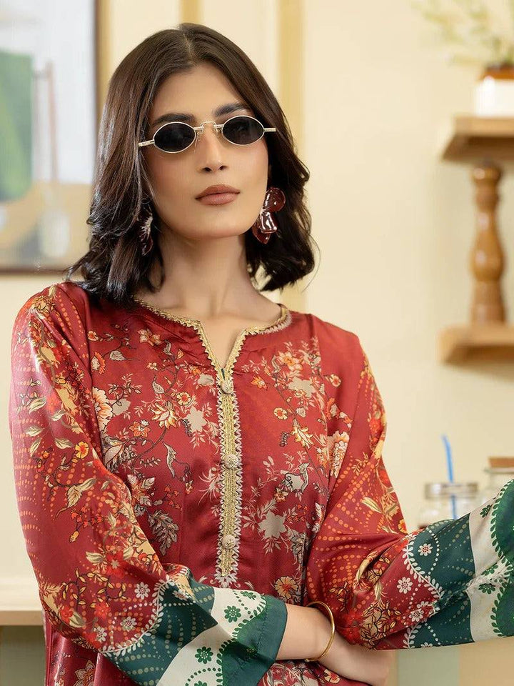 Women in red silk shirt with floral embroidery, accessorized with sunglasses and earrings, standing indoors with a blurred background