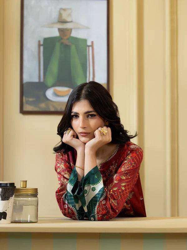 Women wearing traditional red and green embroidered silk shirt with floral patterns, sitting indoors with a painting in the background